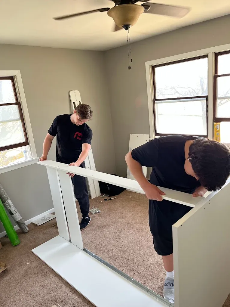 Two movers in black shirts handling white furniture in a residential move