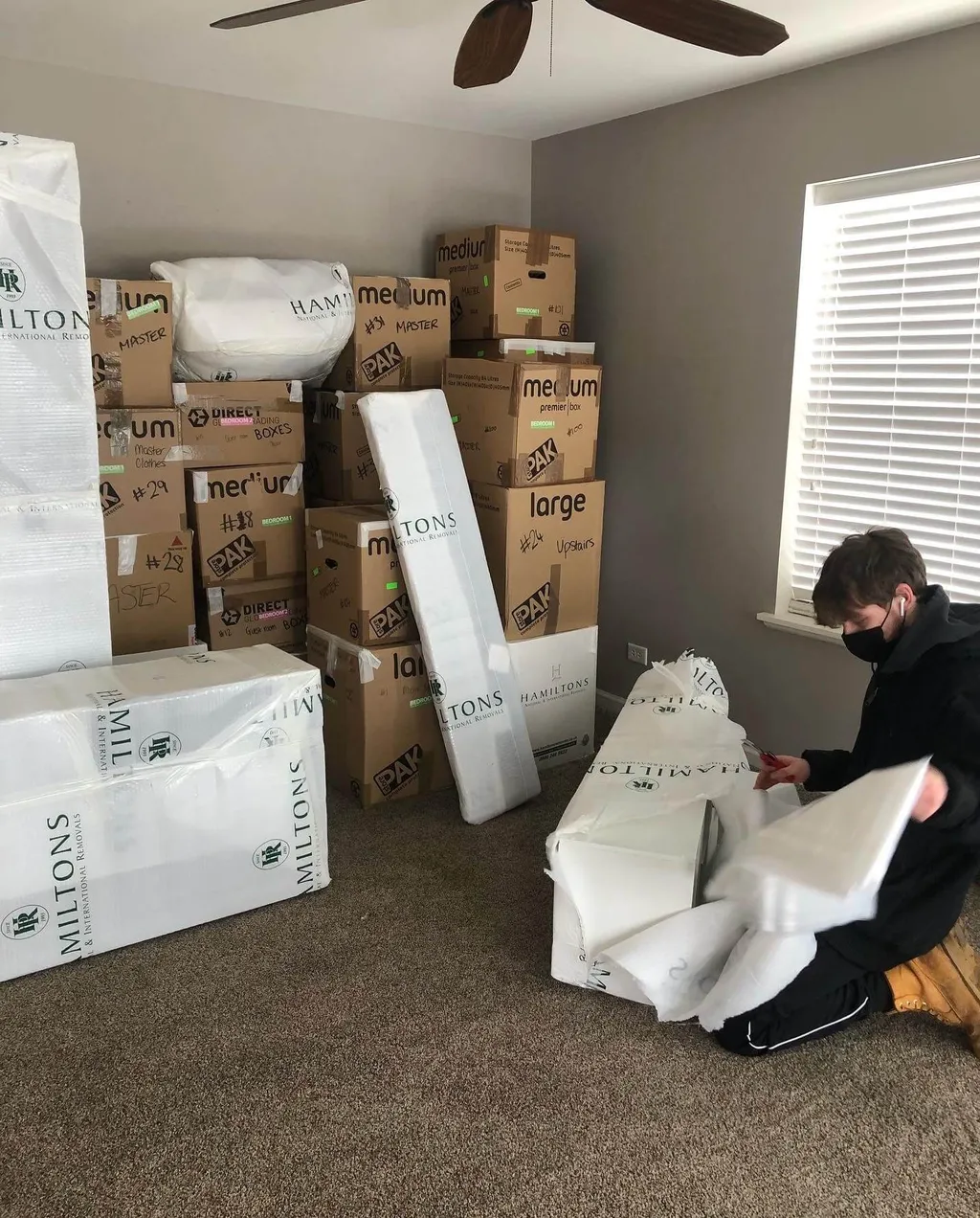 Monolith mover carefully unpacking plastic-wrapped furniture surrounded by labeled moving boxes