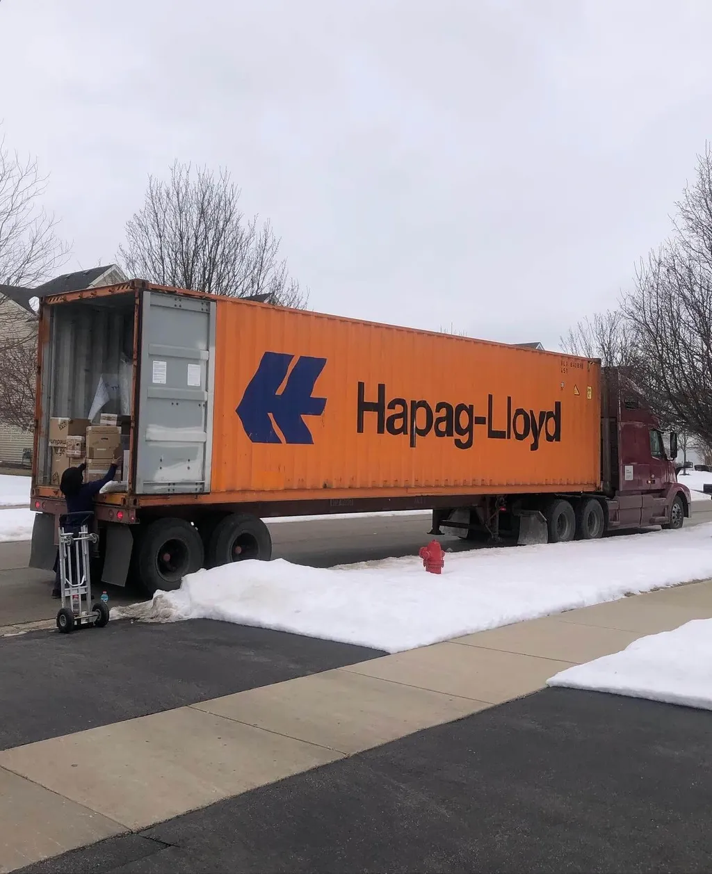 Orange shipping container on a flatbed truck being unloaded at a residential commercial move